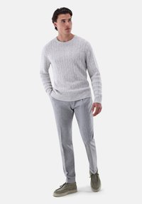 Grauer strukturierter Pullover mit erhabenem Muster, kombiniert mit hellgrauen maßgeschneiderten Hosen und grauen Wildlederschuhen. Einfaches, modernes Design.