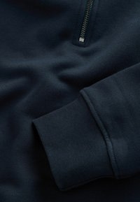Navyblauwe sweatshirtstof met een ritskraag. Glad textuur, ribbelige manchetten en schone stiksels zichtbaar.