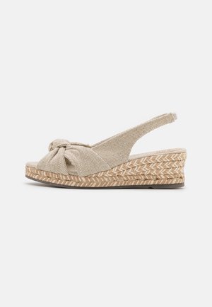 Beżowe sandały na koturnie z tkaniny, z wiązanym detalem z przodu i podeszwą owiniętą jutą. Design z zapięciem na pięcie z teksturowanym wykończeniem.