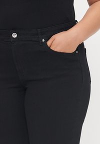 Black jeans made of denim with a smooth texture. Features include a front pocket, silver button, and stitching across the waistband.