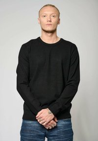 Pull en maille noir à manches longues, col rond et ourlet côtelé. Porté avec un jean en denim bleu. Texture lisse, silhouette ajustée.