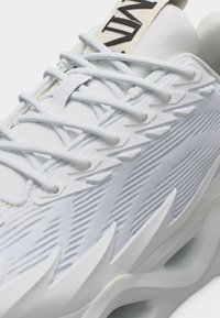 Κοντινή λήψη λευκού αθλητικού παπουτσιού με υφή στο πλάι, κορδόνια σε ζιγκ-ζαγκ και παχιά επενδεδυμένη σόλα.