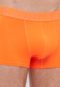 Oranžne bokserice iz gladkega, raztegljivega materiala z kontrastnim BJORN logotipom na elastičnem pasu. Imajo prilegajočo se zasnovo in teksturiran vzorec.