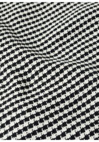 Tissu pied-de-poule noir et blanc avec une surface texturée légèrement froissée.