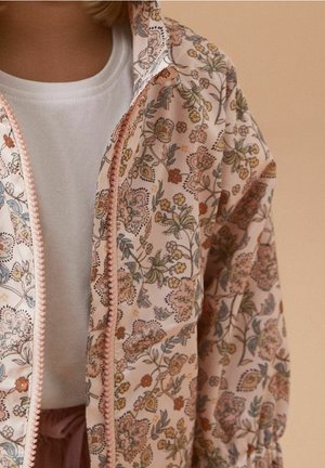 Veste rose à motif floral en tissu léger, dotée d'une fermeture éclair avec un bord texturé et de poignets de manche froncés.