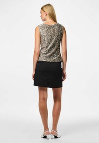 Top na ramiączkach z cekinami w jasnym złocie, dopasowany kształt, w połączeniu z czarną spódnicą. Modelka nosi srebrne buty na obcasie. Gładka tekstura materiału.