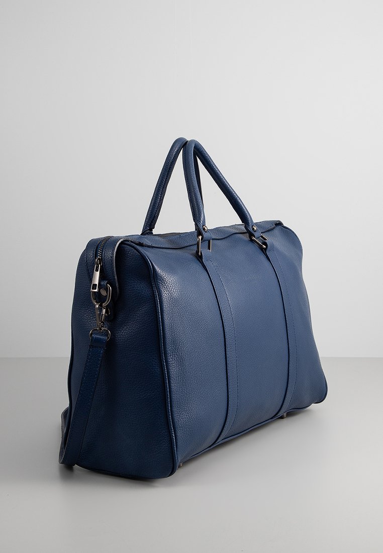 Blaues Leder-Duffelbag mit zwei Obergriffen, abnehmbaren Schultergurt und kontrastierenden vertikalen Nähten an den Seiten. Glatte Textur, geräumiges Design.