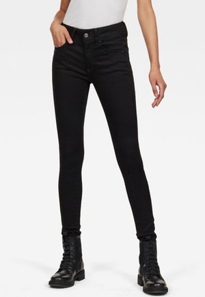 Czarne jeansy slim fit z przednimi kieszeniami, zapięciem na guzik i suwak, noszone z czarnymi wiązanymi botkami za kostkę oraz białym, włożonym do spodni topem.