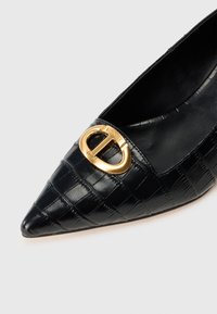 Black pointed-toe shoe made of textured crocodile-embossed leather, featuring a gold circular buckle accent on the vamp.