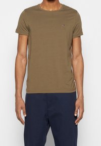 Oliivinvihreä, lyhythihainen t-paita, valmistettu sileästä puuvillakankaasta. Paidassa on hillitty logo rinnassa ja klassinen pyöreä pääntie.