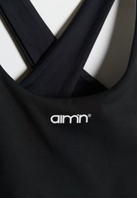 Svart sports tanktop med kryssryggdesign, laget av glatt stoff, med en hvit logo på forsiden.
