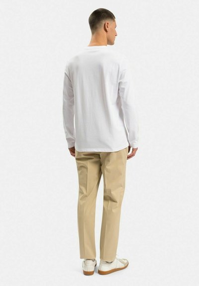 Hvid skjorte med lange ærmer præsenteret med beige bukser og hvide sneakers. Fokus på casual pasform og glat stofstruktur.