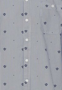 Chemise rayée bleue et blanche avec de petits motifs floraux brodés, devant à boutons et poche. Fabriquée en tissu léger.