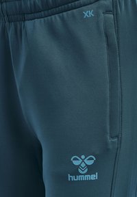 Teal sportieve broek met een gladde textuur. Voorzien van een elastische tailleband, zijzak en een lichtblauw "hummel"-logo.