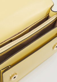 Gul læderhåndtaske med en lynlåslomme. Har en glat tekstur, bronzefarvet hardware og et rent indvendigt design.