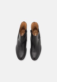 Botas de tobillo de cuero negro con textura suave, punta redondeada, cremalleras laterales y forro interior en tono beige. Diseño limpio sin adornos adicionales.