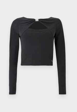 Top corto negro de manga larga con un detalle de corte frontal asegurado por un pequeño adorno de cristal en forma de cuadrado en el escote.