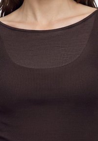 Близък план на човек, носещ плетен тъмнокафяв топ без рамене, показващ областта на врата и ключицата.
