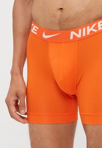 Narančasti elastični bokserice, narejene iz raztegljivega blaga, z belim Nike logotipom na elastičnem pasu. Prilagojen kroj z gladko teksturo brez vidnih vzorcev.