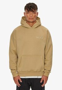 Khaki hoodie made of soft fabric with a front pocket, drawstring hood, and subtle white embroidered logo on the chest. Relaxed fit.