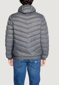 Chaqueta acolchada gris con capucha, patrón de rombos acolchados y cinturilla elástica; combinada con jeans de mezclilla azules.