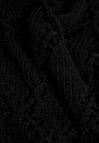 Svart stickad textil med intrikata mönster och upphöjda texturer, inklusive flätade sektioner och ribbade detaljer, tätt vävt tyg.