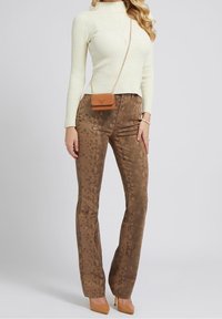Pull à col roulé côtelé crème, pantalon évasé marron à motif serpent, sac à main marron clair avec bandoulière chaîne, talons hauts beiges, fond neutre.