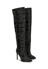 Botas negras de muslo en material suave que presentan patrones de tachuelas blancas y puntas afiladas, con un alto tacón de stiletto.