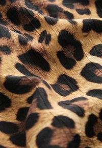 Leopardimusteriga kangas, mis sisaldab kuldse ja musta tooni segu, millel on tekstureeritud pind ja eristuvad mustad laigud pruunikal taustal.
