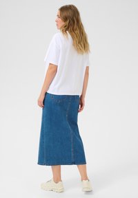 T-shirt en coton blanc associé à une longue jupe en denim. La jupe présente deux poches arrière et une coupe droite, se terminant au-dessus des chevilles.