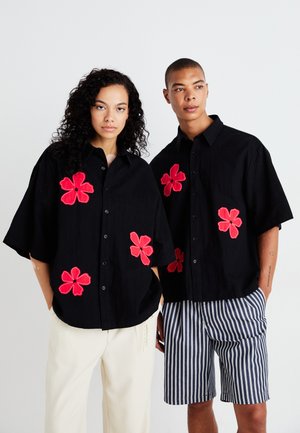 Black button-up shirts with short sleeves, featuring red floral embroidery on the front. The models wear contrasting light and striped shorts.