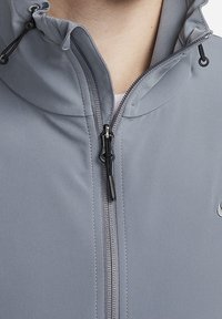 Grijze zip-up jas met hoge kraag, voorzien van een duurzaam weefsel, verstelbare trekkoordcapuchon en zwarte ritsdetails.