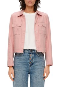 Kürz Jacke in Pink mit Druckknöpfen und zwei Brusttaschen, aus glattem Stoff gefertigt. Tragen über einem weißen Hemd und kombiniert mit hoch taillierten Jeans.