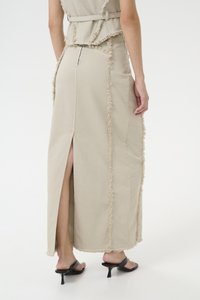 Lys beige denimkjole med frynser, sideslits og lynlås i ryggen. Brukt med svarte hæl sandaler. Glatt tekstur, lang silhuett.