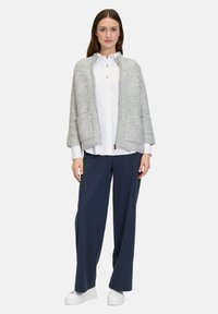 Grau gestrickte Strickjacke mit strukturierter Oberfläche, offenem Vorderteil und seitlichen Taschen, getragen über einem weißen Hemd und marineblauen weiten Hosen.