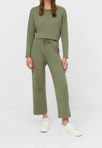 Ensemble en deux pièces de couleur vert olive, à côtes, comprenant un haut court à manches longues et un pantalon à jambes larges, doté d'une taille à cordon et d'un tissu texturé.