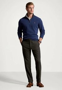 Μπλε φούτερ με φερμουάρ και γκρι κολ�άρο, συνδυασμένο με γκρι μάλλινες παντελόνες και καφέ δερμάτινα παπούτσια. Τα αξεσουάρ περιλαμβάνουν ένα ρολόι.