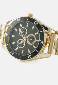Montre dorée avec un cadran noir, dotée d'accents argentés, de trois sous-cadrans et d'un motif texturé. Bracelet en métal de style métal.