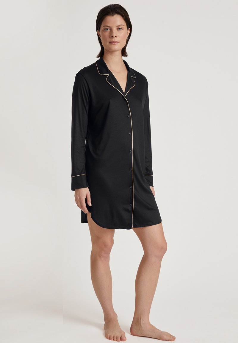 Vestito da pigiama nero con maniche lunghe, bottoni frontali e piping dorato a contrasto lungo il colletto e le maniche. Tessuto morbido e liscio.