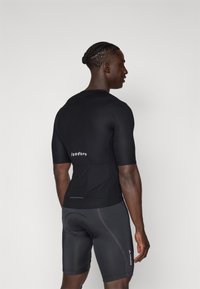Svart sykkelskjorte med korte ermer, strukturert stoff, med baklomme og logoen "Isadore". Kombinert med svarte shorts med sidesømmer.