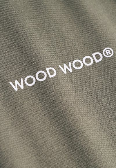 Oliivroheline kangas sileda tekstuuriga, mille keskel on valge "WOOD WOOD®" logo, trükitud rasvases sans-serif fontis.