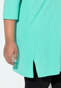 Tunica verde menta con maniche a tre quarti, caratterizzata da spacchi laterali e texture morbida. Abbinata a leggings neri.