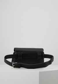 Sac bandoulière en cuir noir avec surface texturée, fermeture à rabat, sangle avec boucle réglable et design minimaliste.