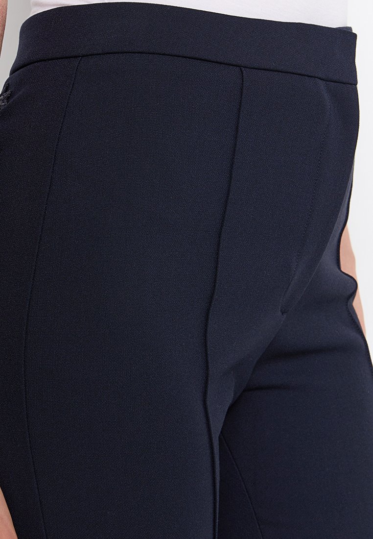 Pantalons bleu marine à coupe ajustée, avec une texture lisse, des lignes de pli subtiles et une taille plate qui met en valeur la silhouette.