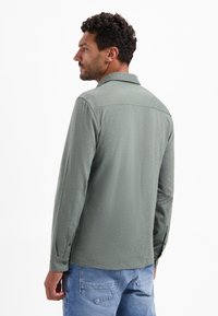 Lange mouwen, lichtgroen shirt in een gestructureerde stof, met een kraag en knoopmanchetten, gecombineerd met een blauwe spijkerbroek.