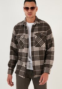 Cămașă din flanela în carouri maro și alb, cu un design cu nasturi, două buzunare pe piept și o textură moale. Purtați-o peste un tricou alb.
