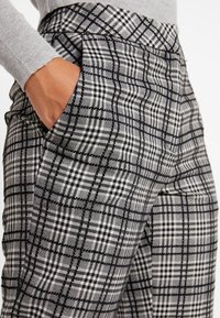 Harmaat ja valkoiset ruudulliset housut, joissa on muotoiltu istuvuus. Ne sisältävät litteän etuosan, sivutaskut ja teksturoidun kankaan, jossa on hienovarainen kiilto.