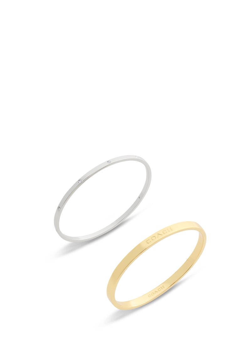 Par de pulseras: una de plata con pequeños cristales transparentes, una de oro con el nombre de la marca grabado. Ambas tienen un diseño delicado y suave.