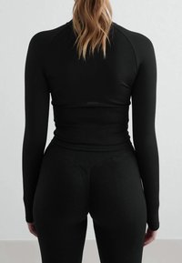 Haut noir à manches longues et leggings en tissu extensible, avec une texture côtelée et une coupe ajustée pour une utilisation en vêtements de sport.