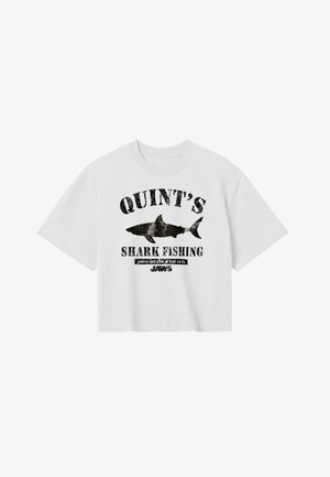 Camiseta blanca recortada con texto gráfico negro que dice "QUINT'S SHARK FISHING" junto a una silueta negra de un tiburón y la palabra "JAWS" debajo.